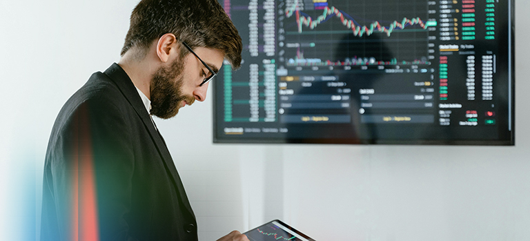 Personne avec tablette devant grand écran affichant des graphiques financiers – investissements et analyse business