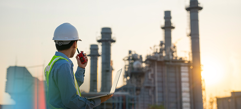 Ingénieur avec ordinateur portable et radio devant une installation industrielle – sécurité, ingénierie et production